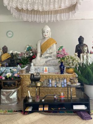 A Buddhist shrine with a central marble statue of Buddha surrounded by other statues and candles and flowers